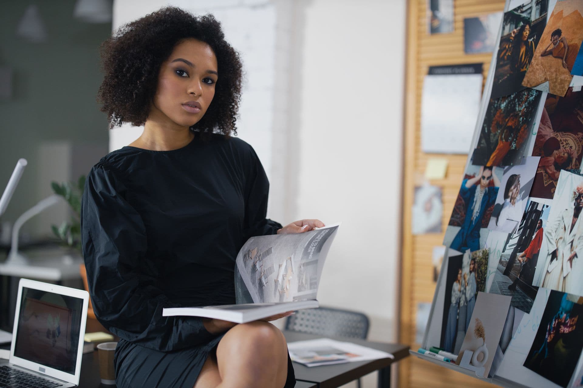 An editor in a black dress sits with an open magazine in a studio lined with issues